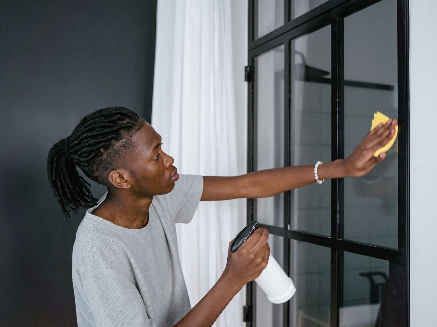 Cleaner spraying and wiping a window at home